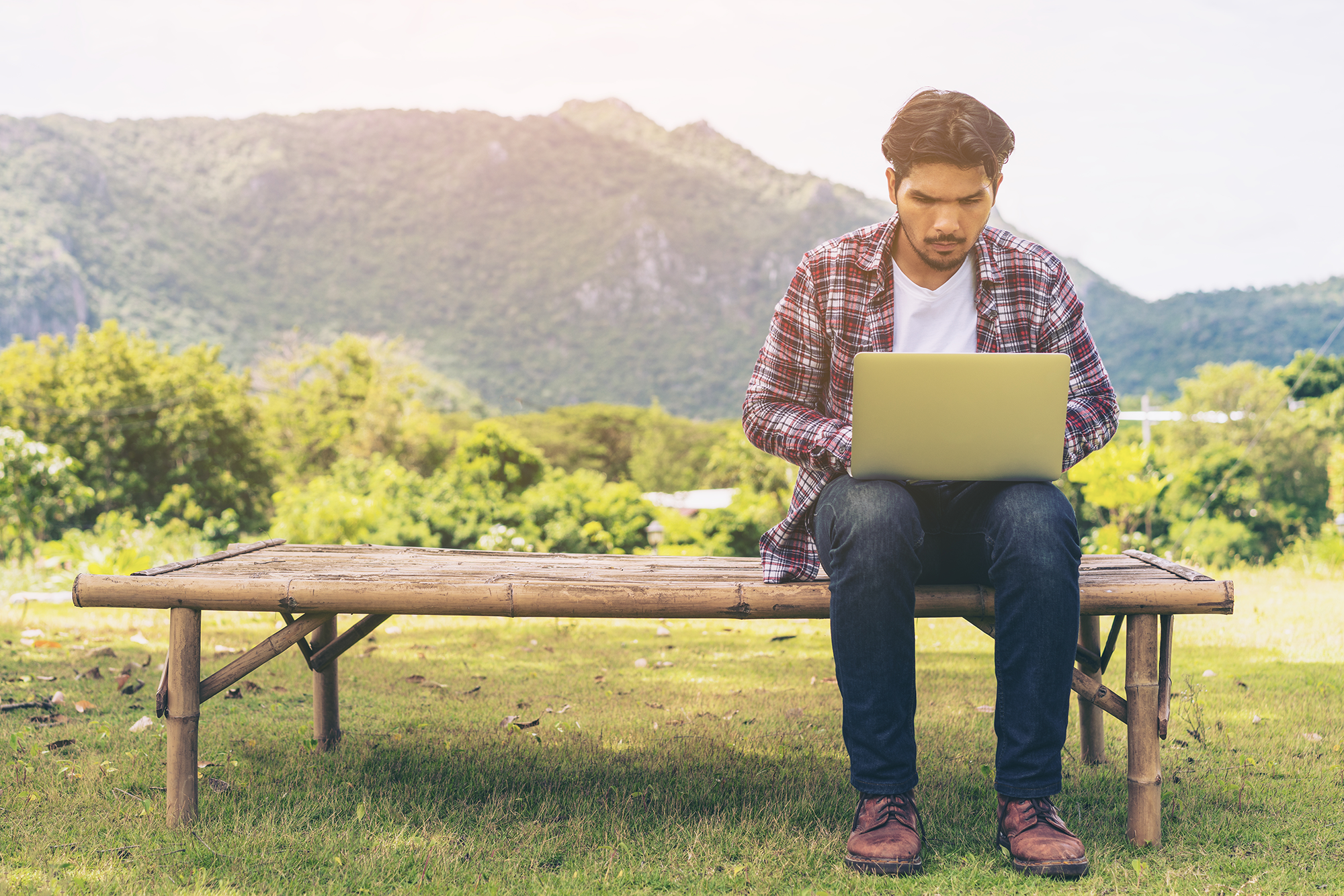 Mann sitzt mit einem Laptop auf einer Bank im grünen