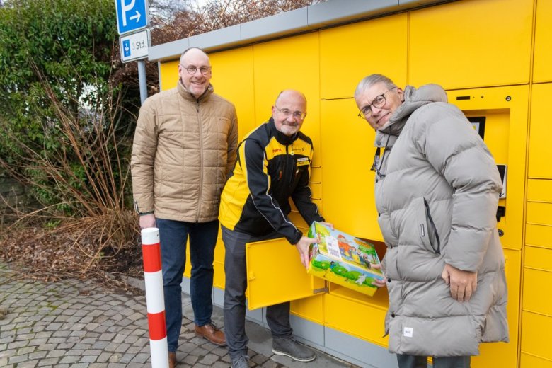 Andreas Hermanns, Peter Mayer und Bürgermeister Bernd Goffart mit einem bunten Paket vor der Poststation