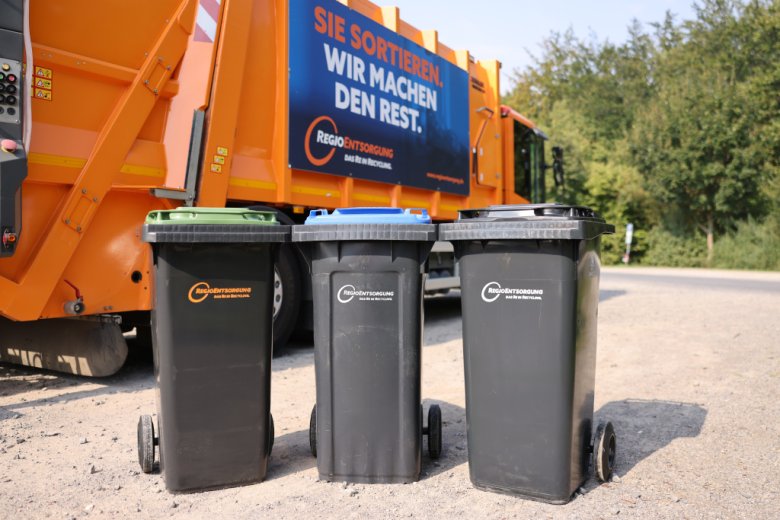Drei Mülltonnen vor einem Abfuhrfahrzeug