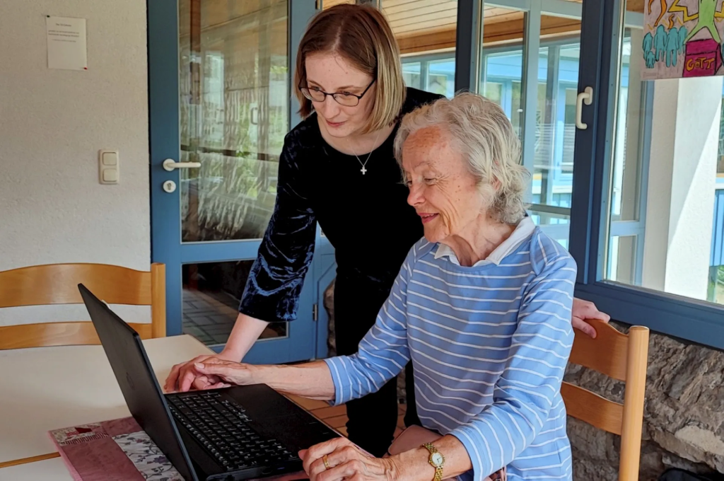 Helferin unterstützt Seniorin am PC
